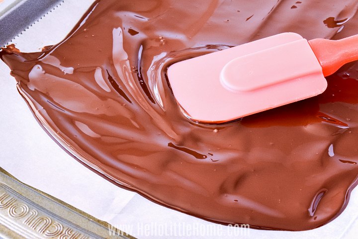 Spreading melted chocolate on a lined baking sheet with a spatula.