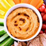 A bowl of spicy chipotle hummus surrounded by veggies and pita.
