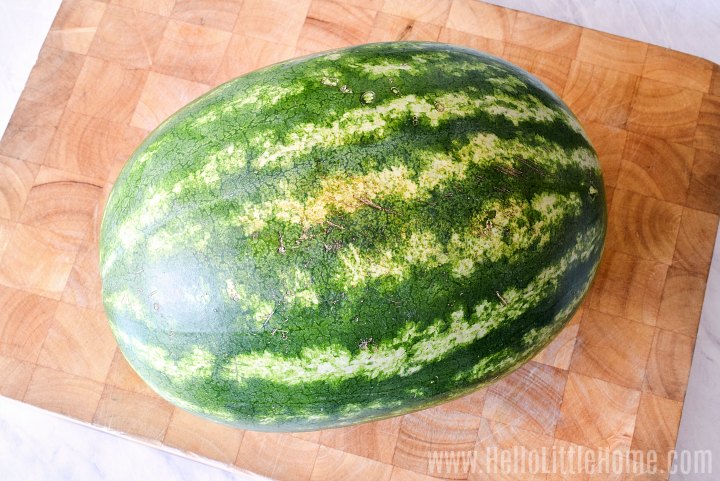 A whole watermelon on a wood cutting board.