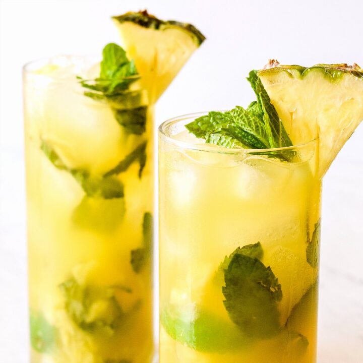 Two Pineapple Mojitos garnished with mint and fruit wedges.