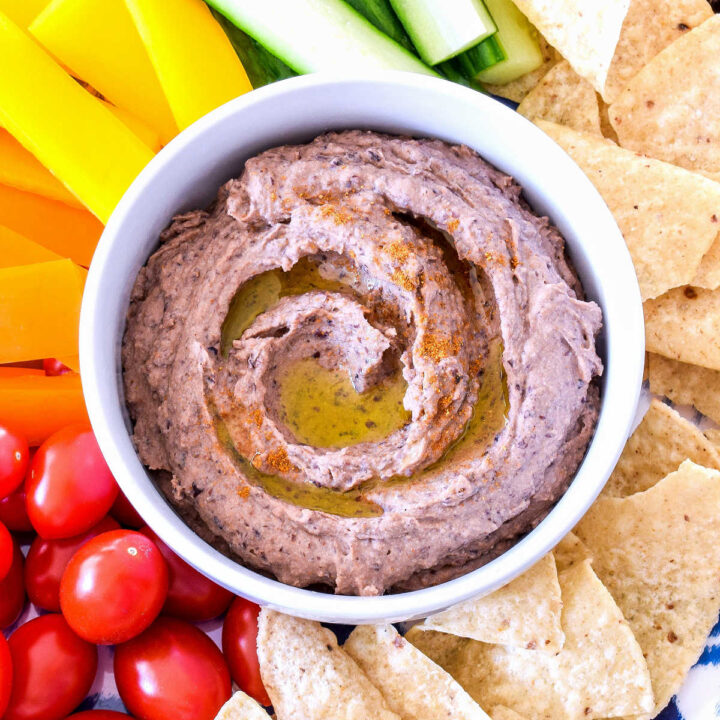 A bowl of black bean hummus surrounded by veggies and tortilla chips.