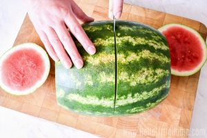 Slicing a watermelon in half on a wood cutting board.