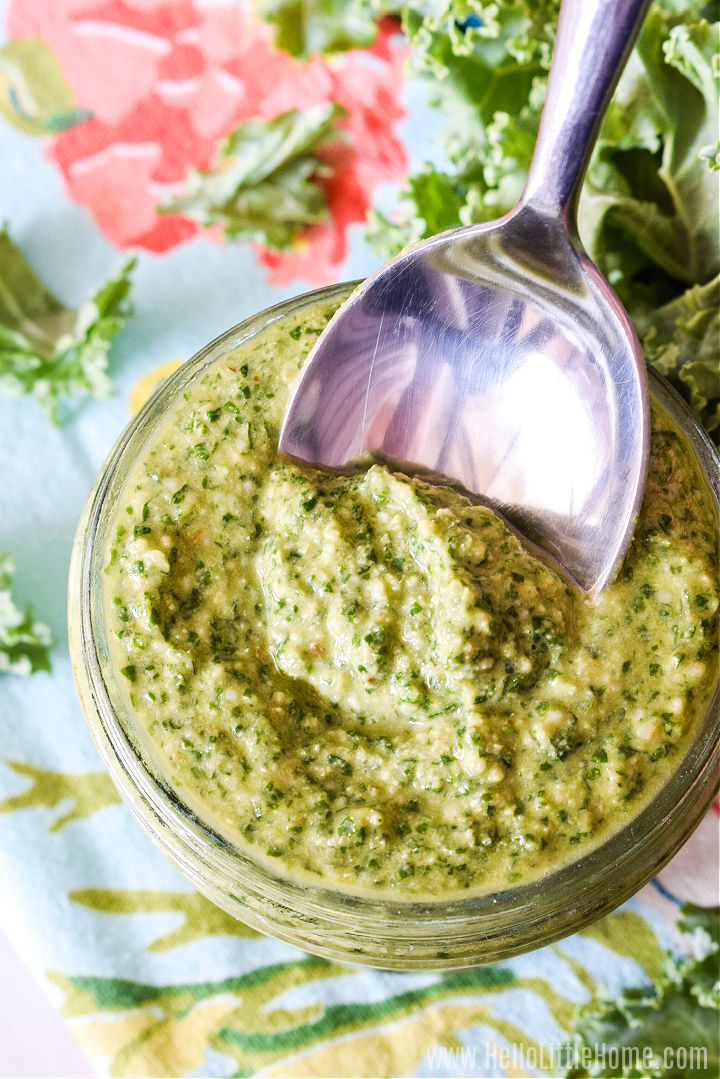 A spoon scooping kale walnut pesto out of a jar with a floral napkin in the background.