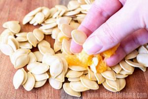 A hand separating raw pumpkin seeds from the pulp.