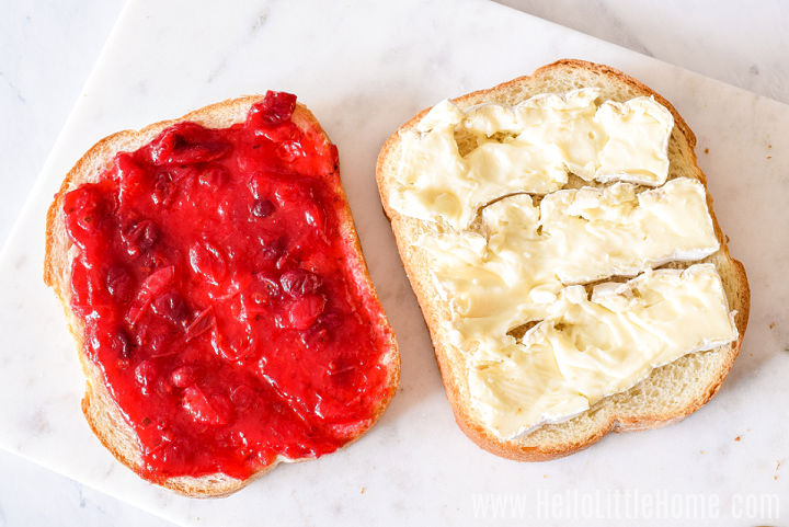 Two pieces of bread, one topped with cranberry sauce, and the other topped with brie.
