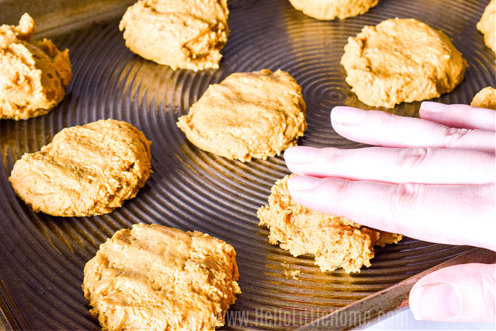 A hand pressing a cookie on a baking sheet.