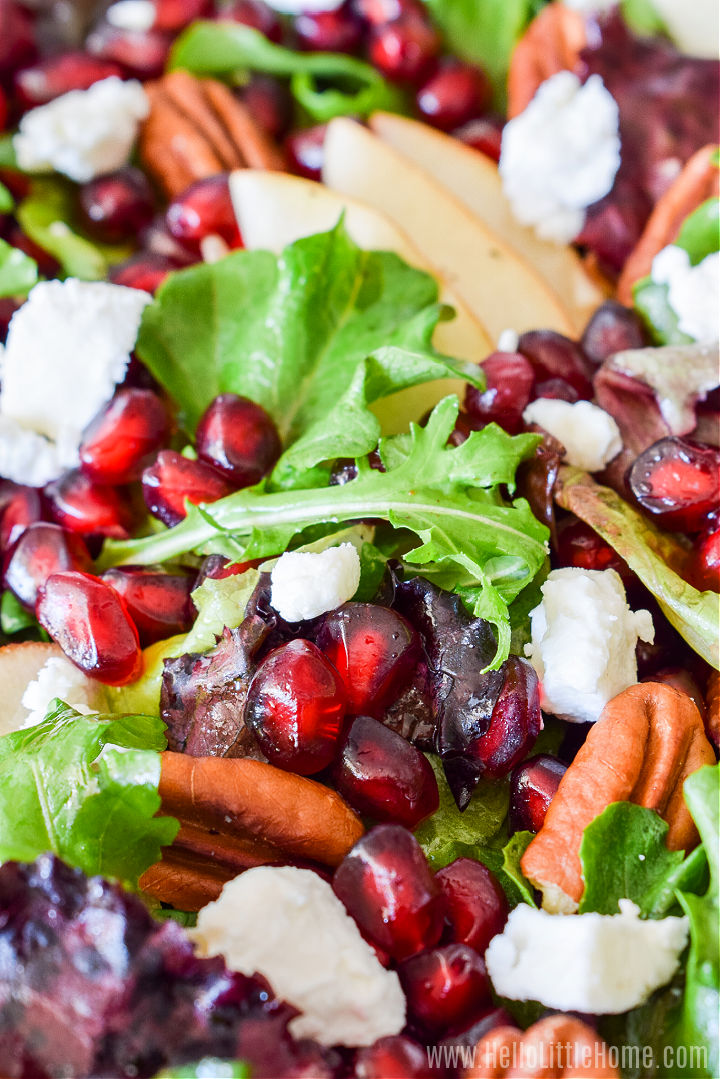 Closeup of the finished green salad with pomegranate seeds, goat cheese, pears, and pecans.