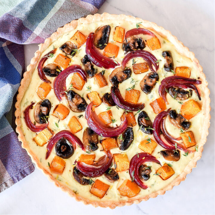 A Roasted Vegetable Tart and a plaid napkin on a marble counter.