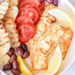 Feta Saganaki, tomatoes, bread, olives, and lemon wedges on a platter.