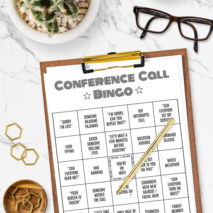 Printable Conference Call Bingo Card on a clipboard surrounded by paper clips, eye glasses, and a small plant.