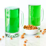 Two Green Beers served in mugs next to a bowl of peanuts.