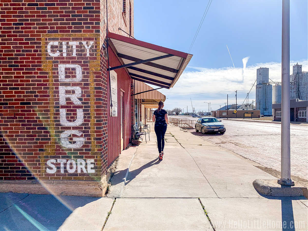 A woman running along a sidewalk in front of a brick store.