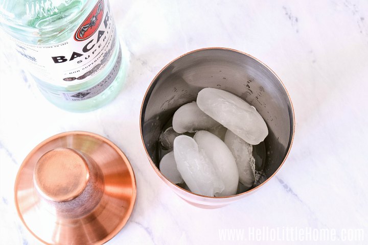 A bottle of rum and a cocktail shaker filled with ice on a marble counter.