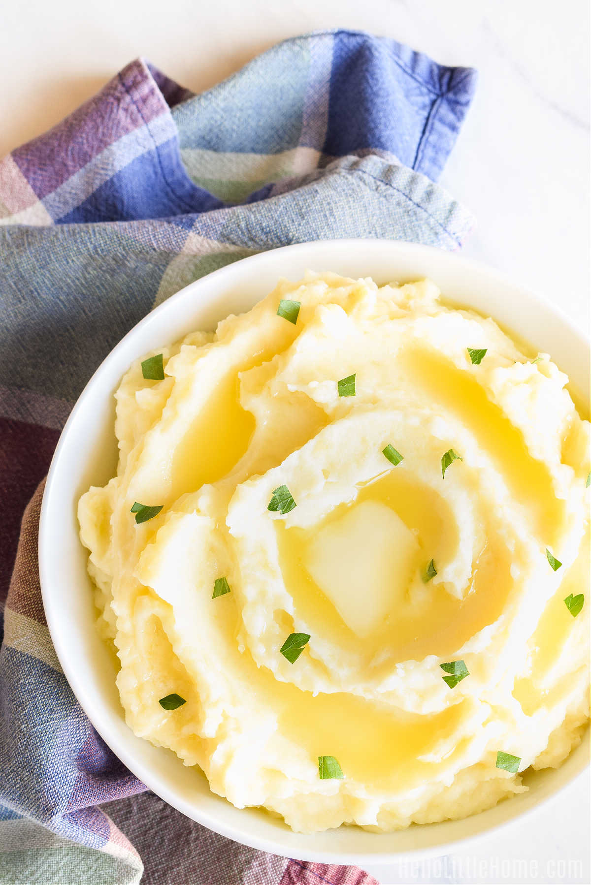A bowl of potatoes topped with butter next to a plaid napkin.