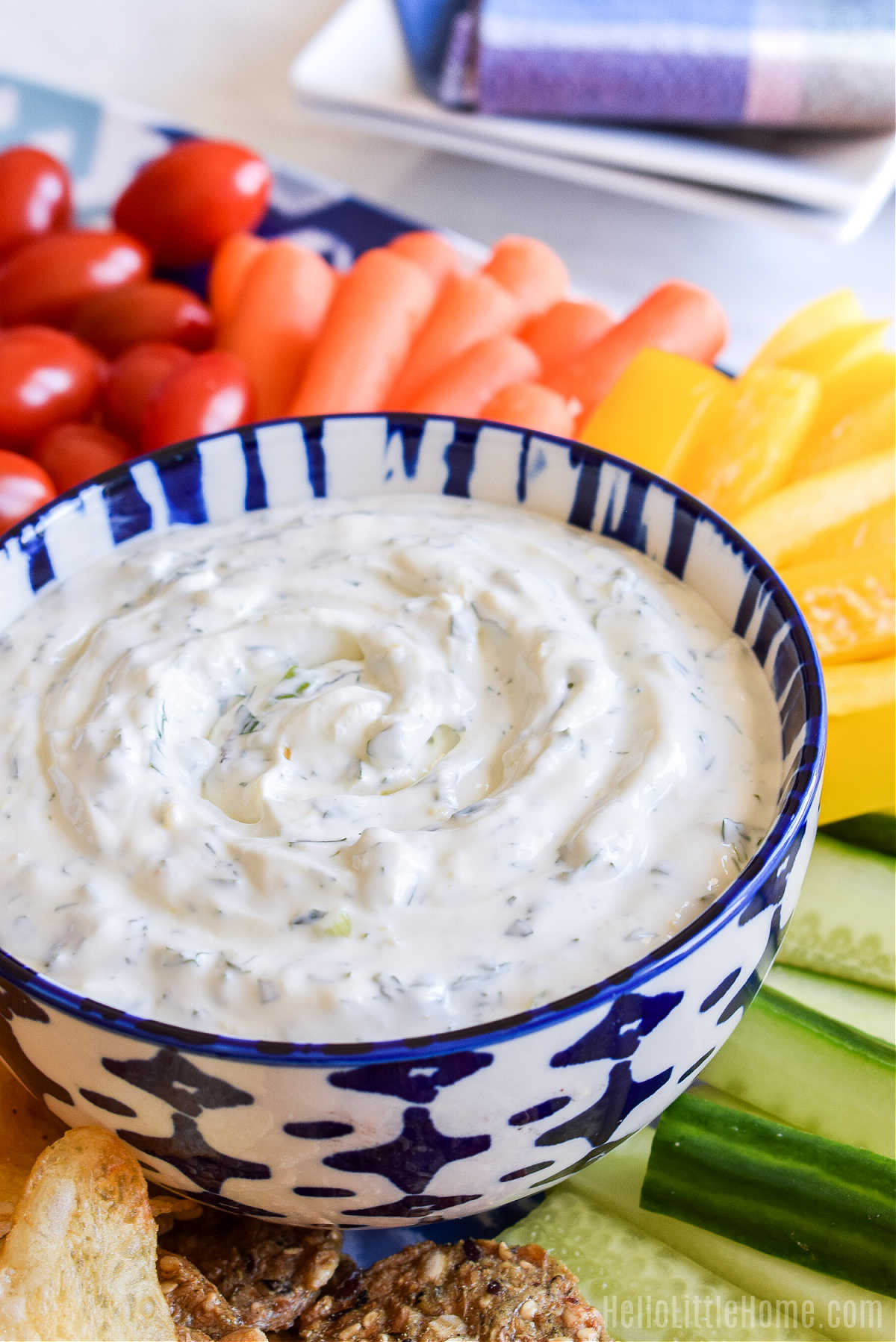 A bowl of Garlic Herb Dip with veggies and plates in the background.
