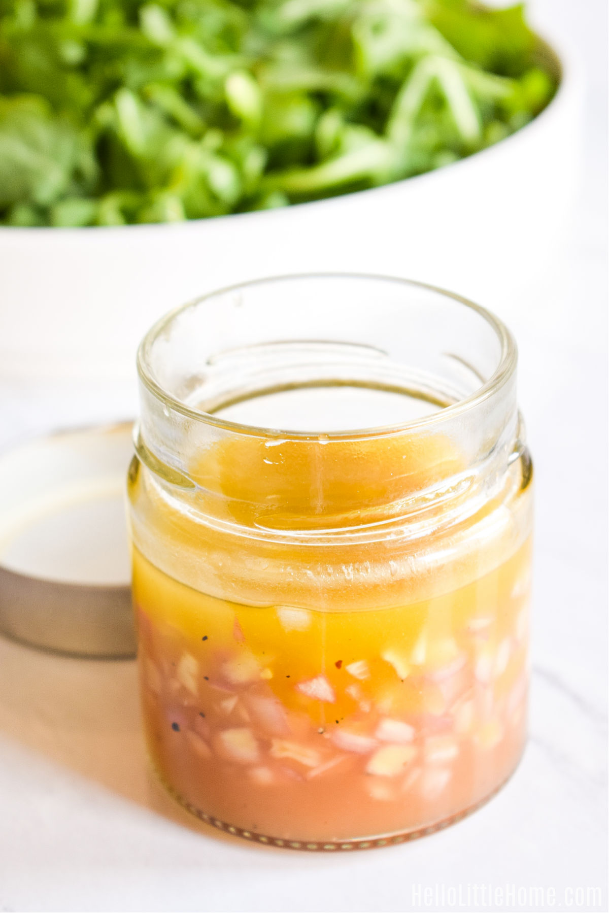 A jar of the finished vinaigrette next to a bowl of lettuce.