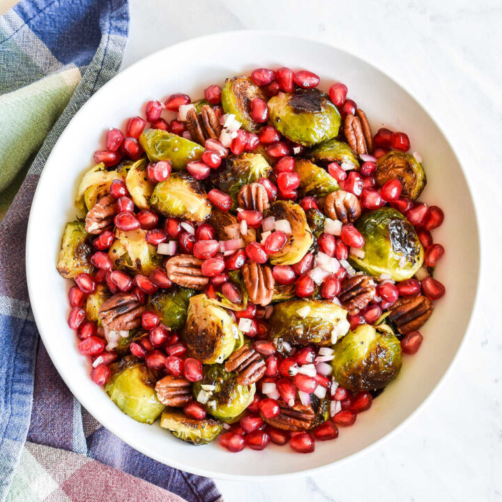 A bowl of Roasted Brussels Sprouts with Pomegranate Seeds next to a plaid napkin.