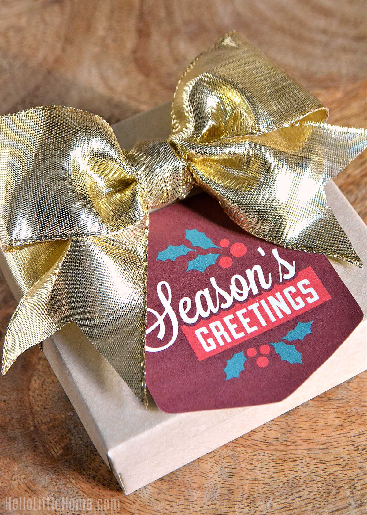 A small box topped with a Christmas Greetings Tag and a gold bow.