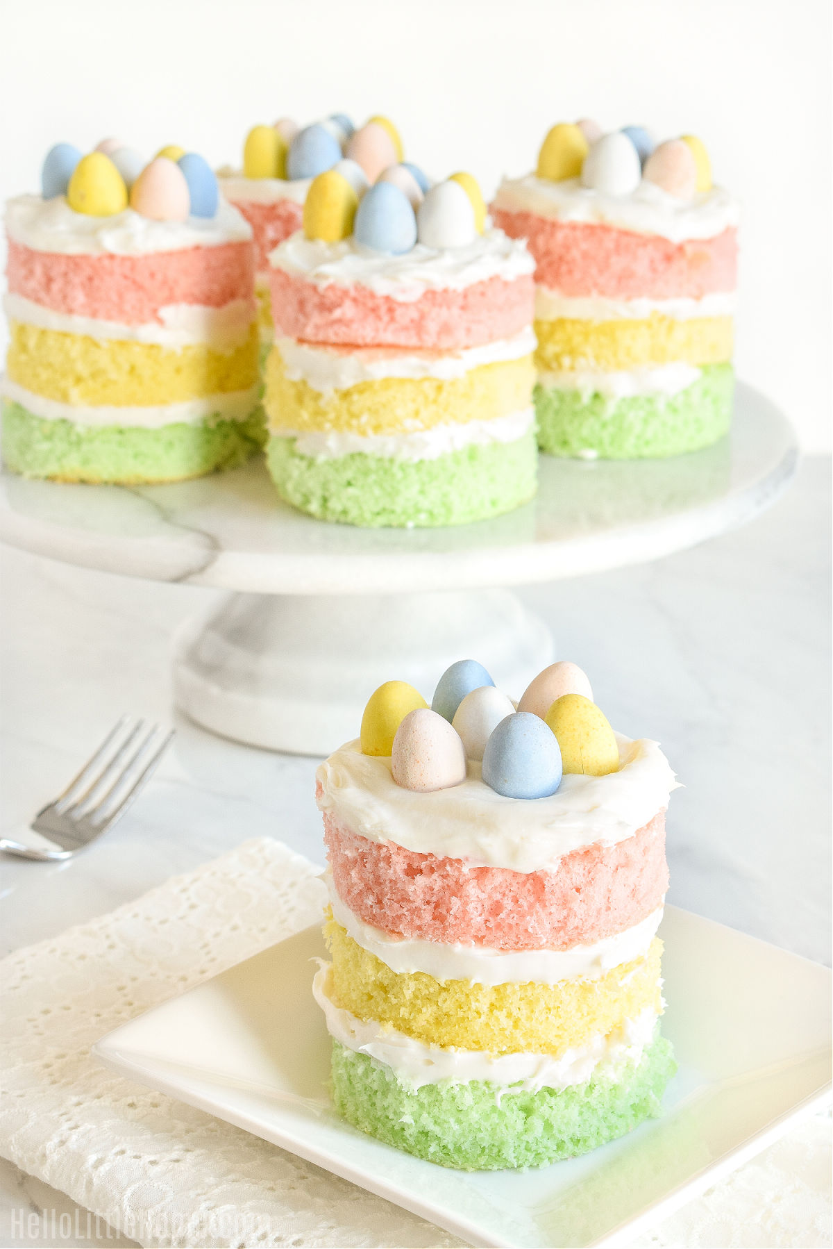 An individual cake decorated with Cadbury Mini Eggs with more cakes on a pedestal in the background.