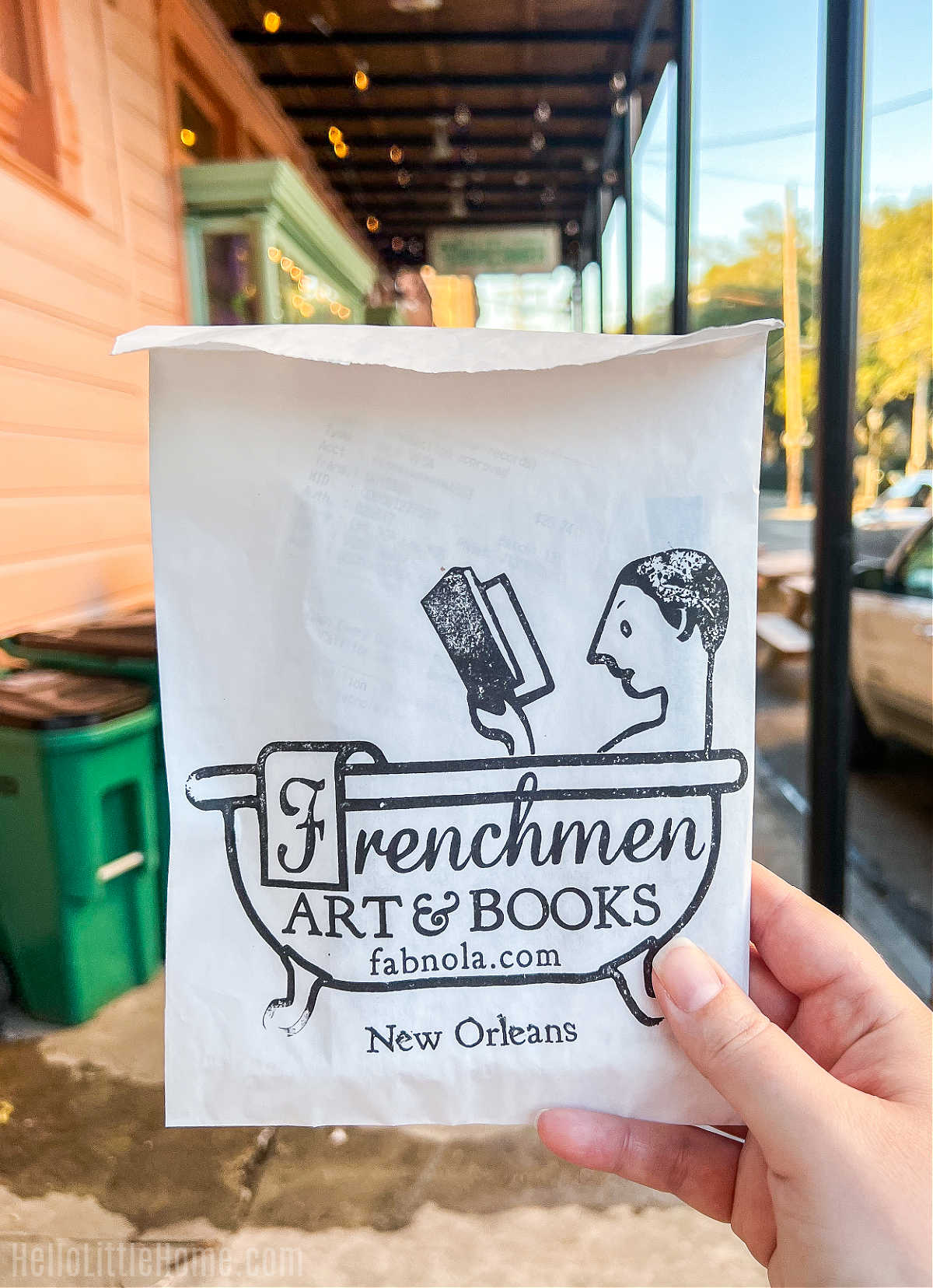 A hand holding a bag from Frenchmen Art & Books in front of a colorful street.