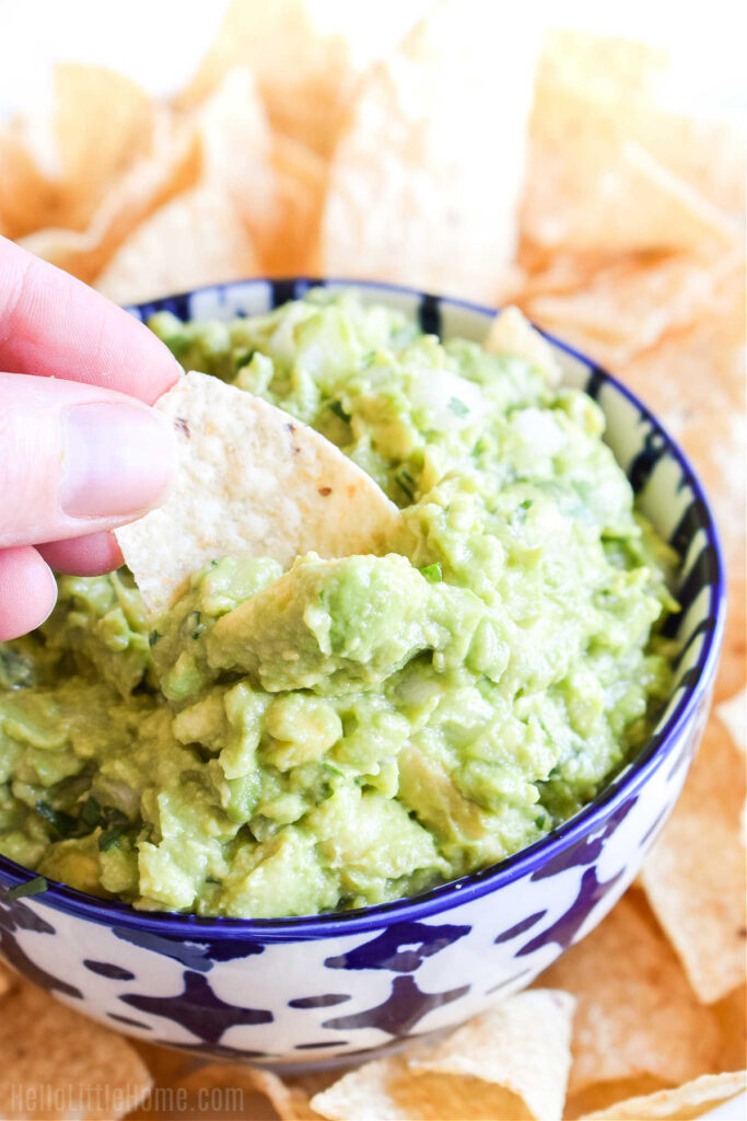A hand dipping a chip in a bowl of the finished dip.
