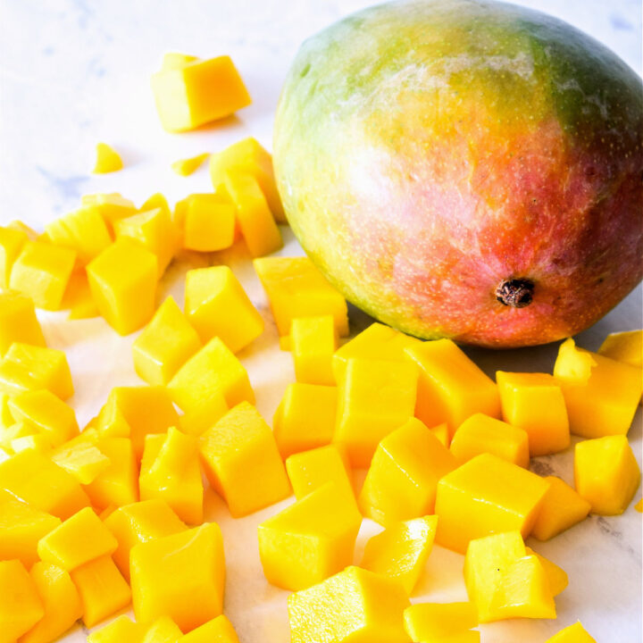 Chopped mango and a whole mango on a marble counter.