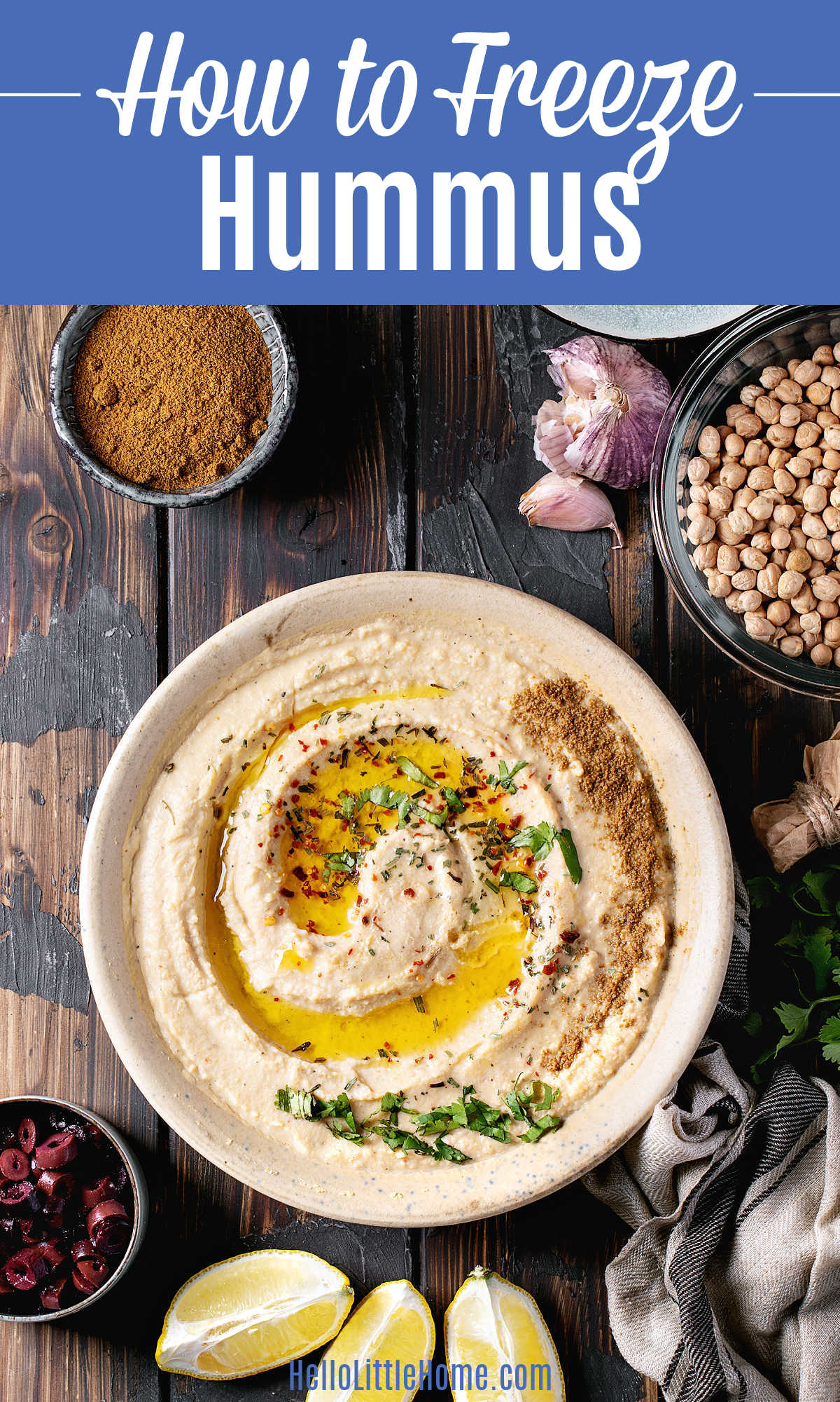 A bowl of hummus on a dark wood table surrounded by the ingredients to make it.