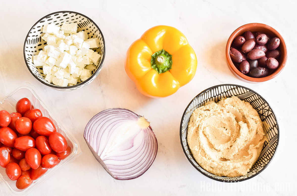 Hummus pizza ingredients arranged on a marble counter.