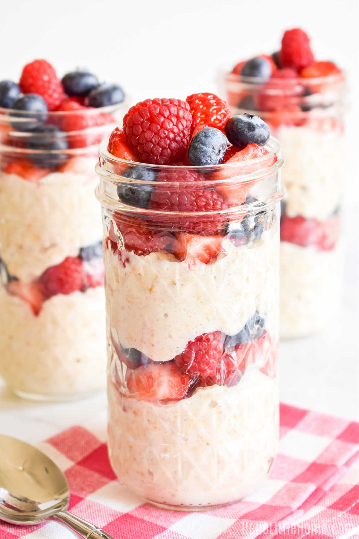 Three jars of oats with yogurt and fruit on a counter.