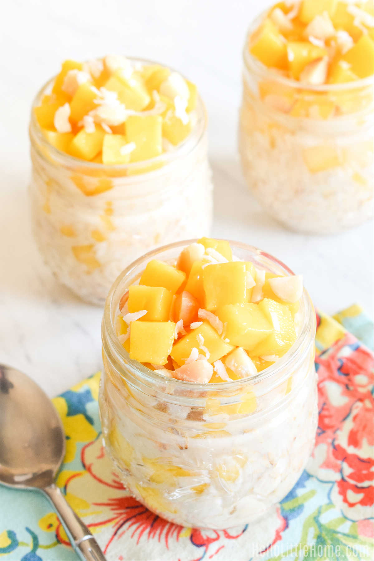 Three jars of overnight oats topped with mango on a marble counter.