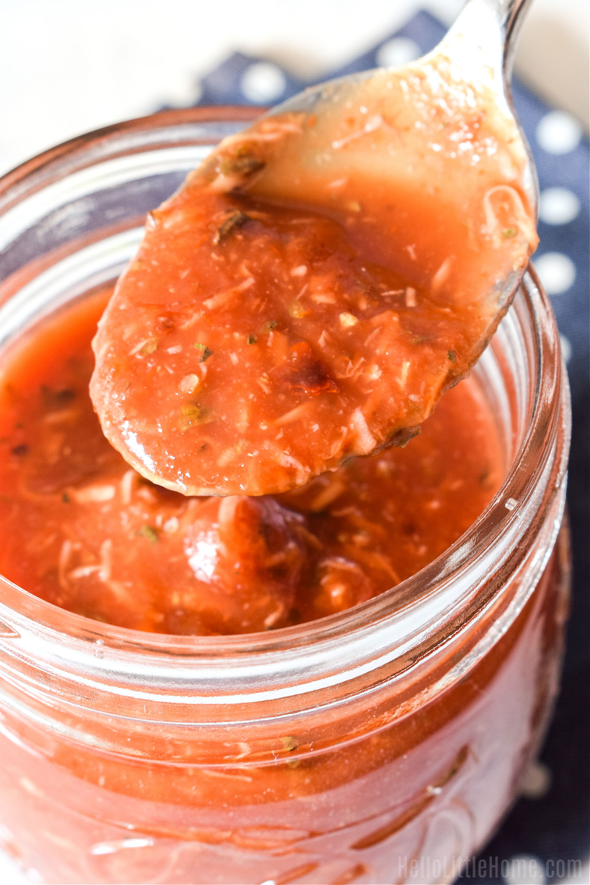 A spoon filled with pizza sauce hovering over a jar of the sauce.