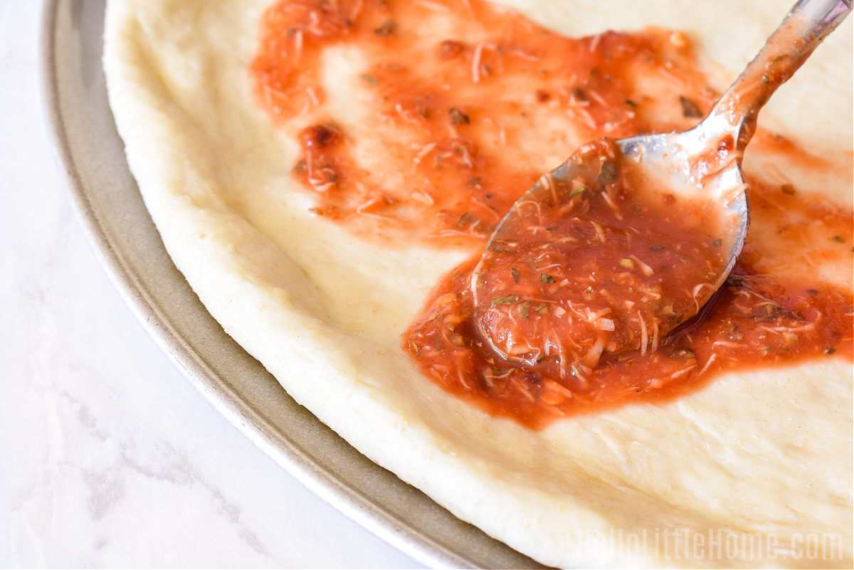 A spoon spreading sauce on a pizza crust.