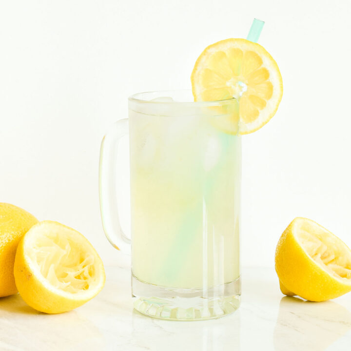 A glass of Single Serving Lemonade surrounded by lemons on a marble counter.