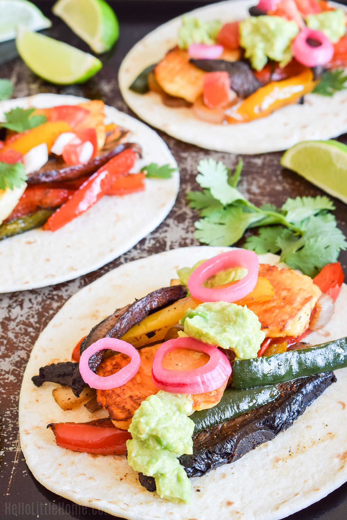 A tray of the finished fajitas served with fresh cilantro and lime wedges.