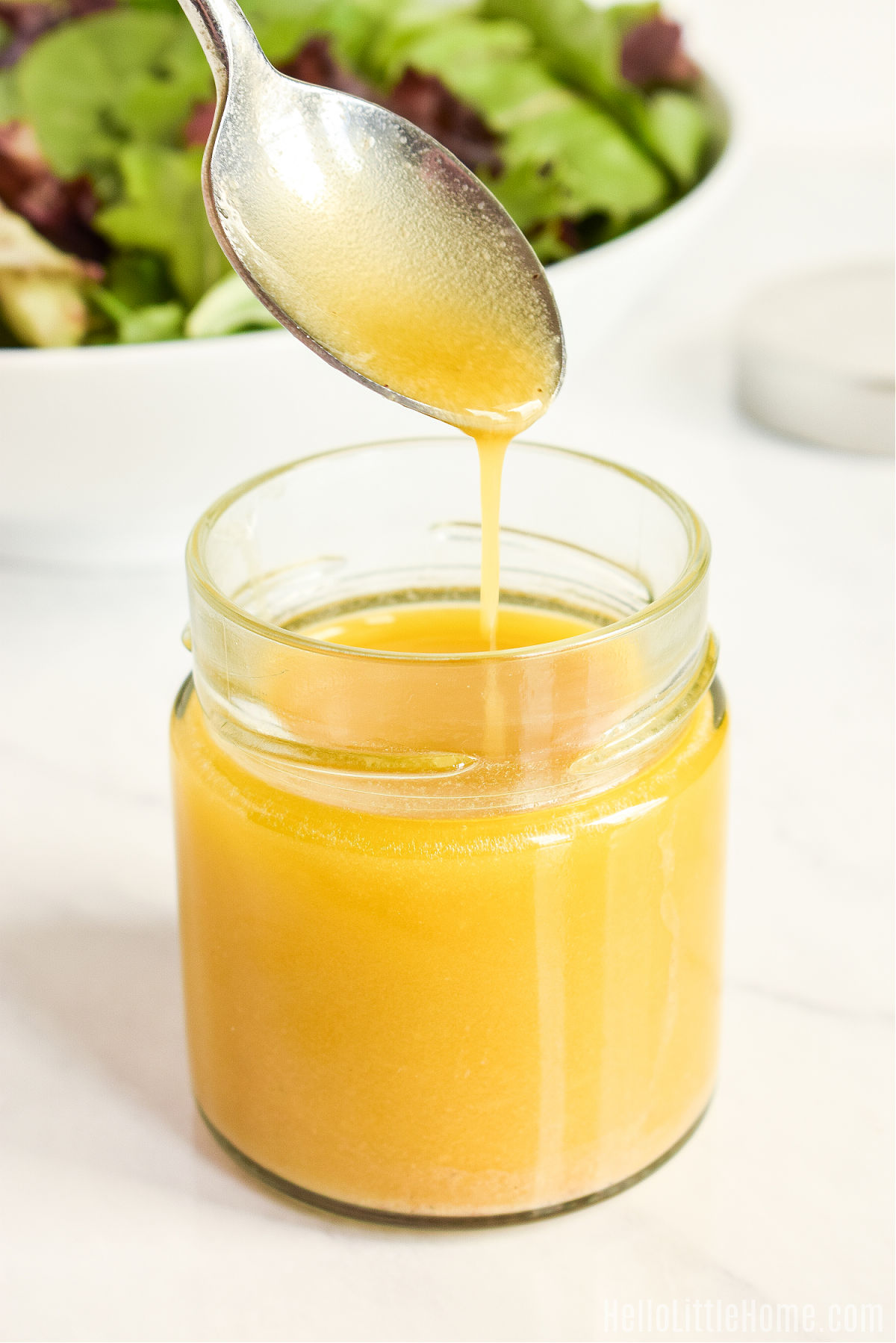 A spoon drizzling the finished vinaigrette into a jar.