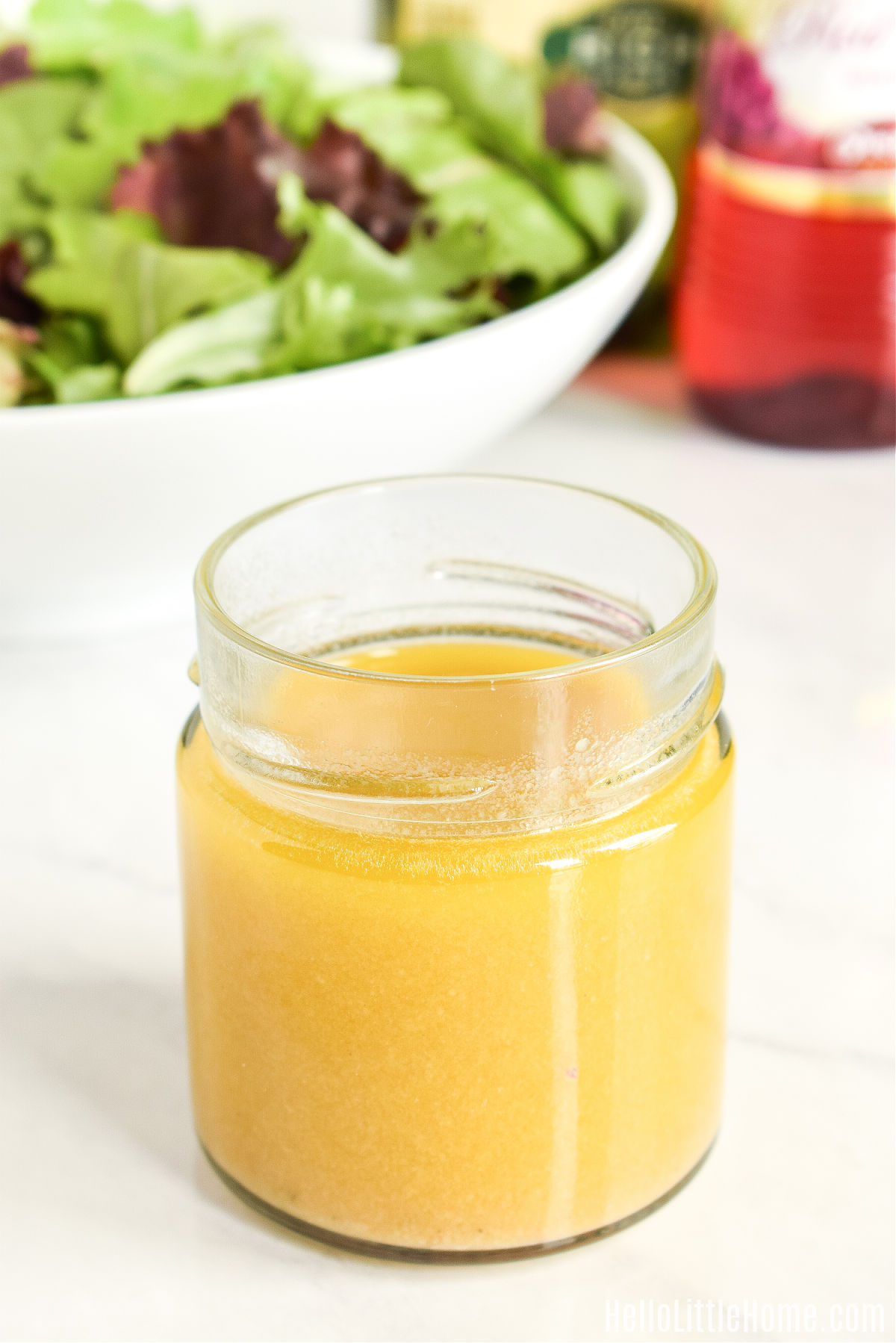 Vinegar and oil dressing in a jar in front of a salad.