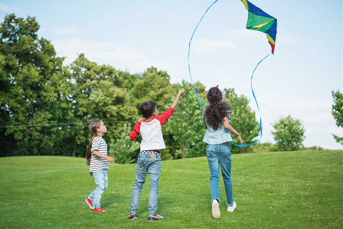 Three children flying a kite on a grassy field.