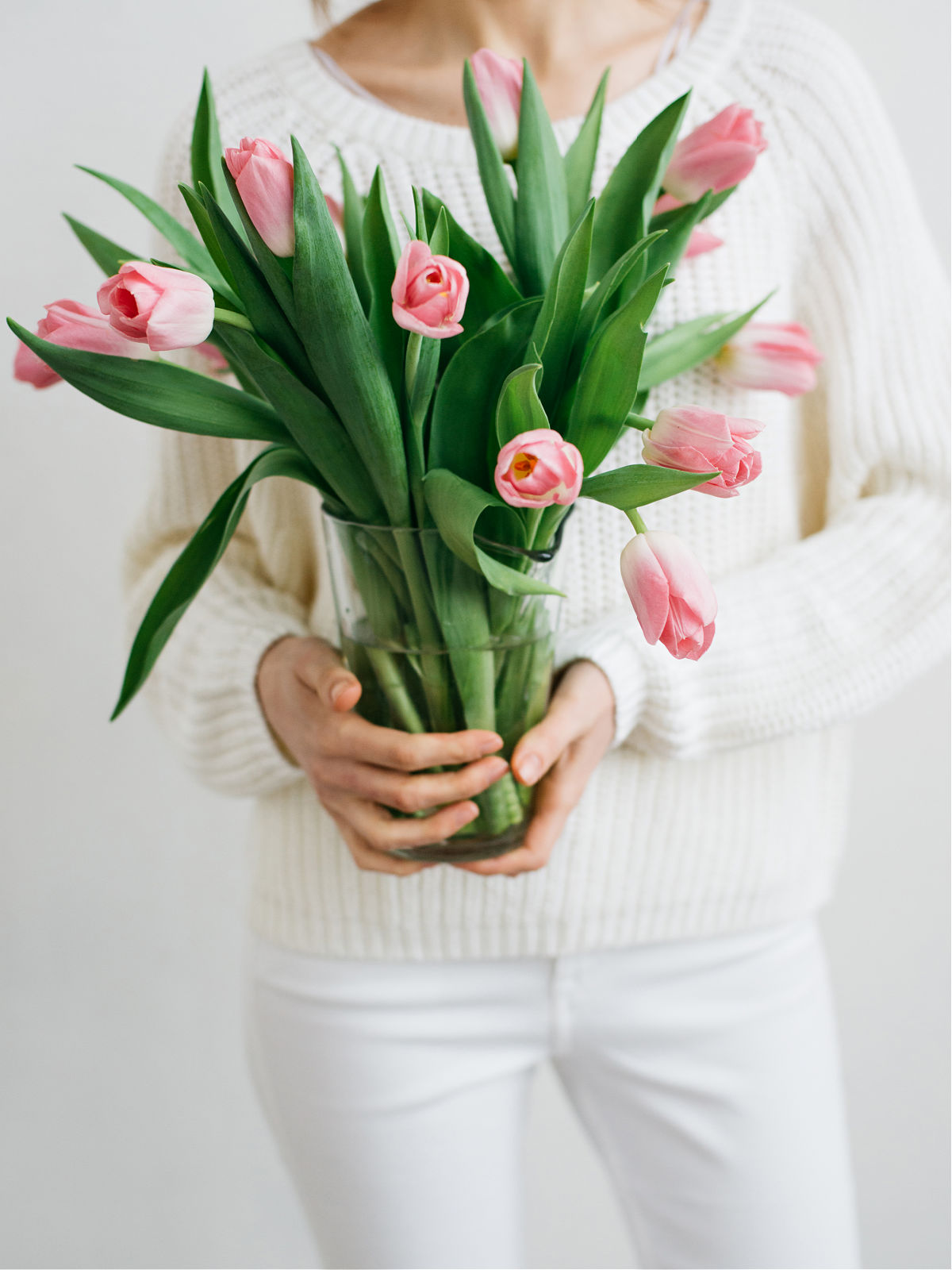 A woman holding a vase filled with spring tulips.