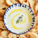 A bowl of Whipped Goat Cheese surrounded by bread slices.