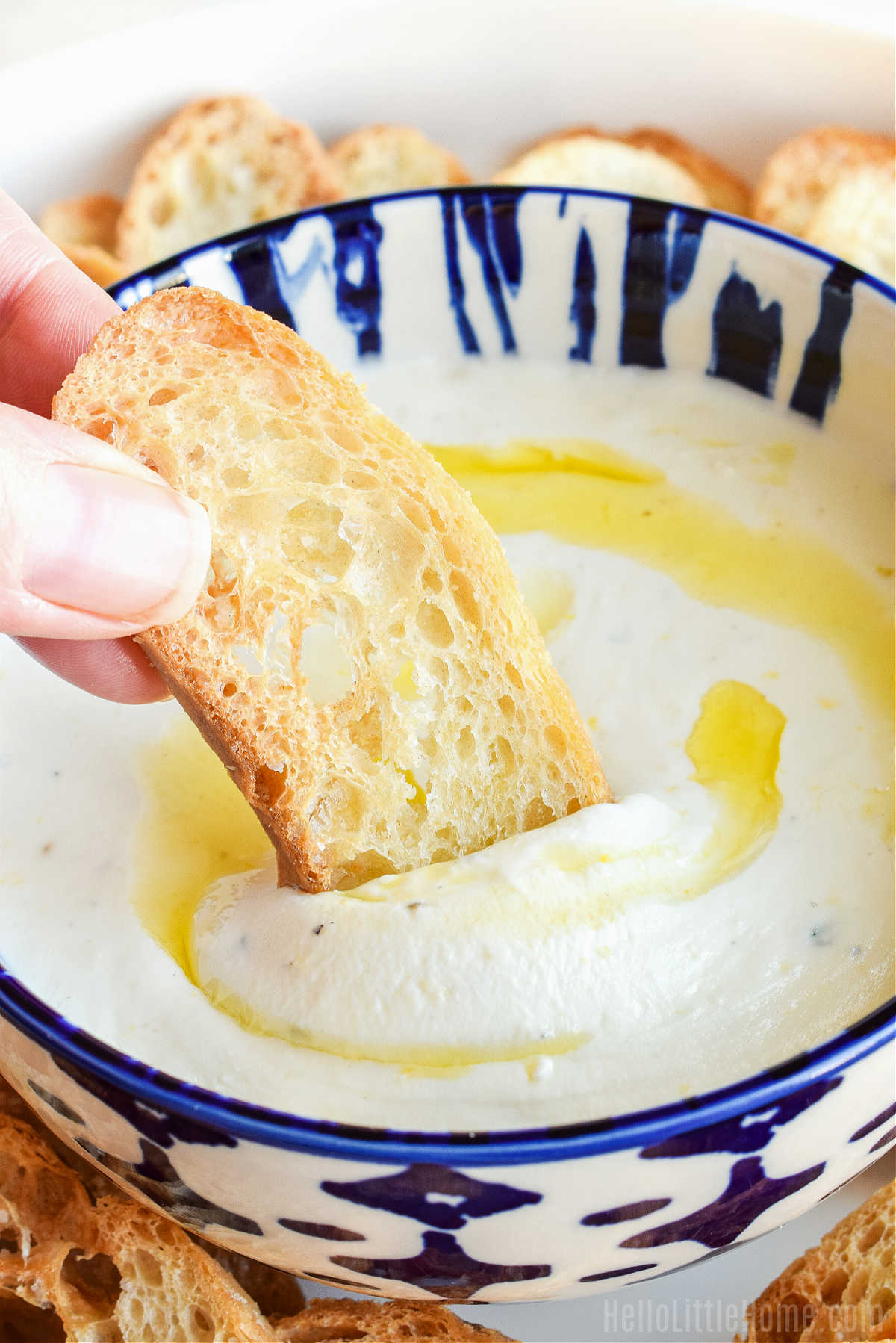 A hand scooping up the dip with crostini.