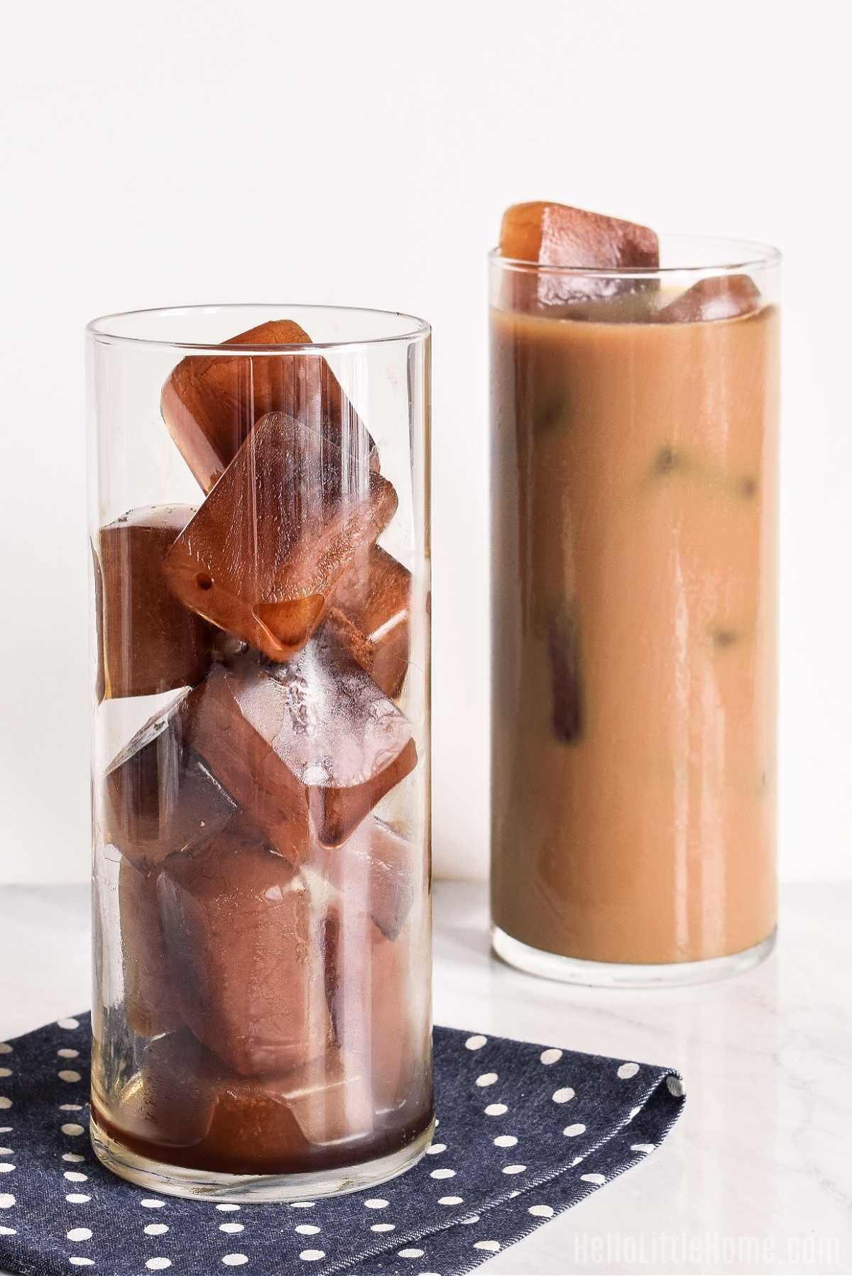 A glass filled with ice cubes with an iced coffee behind it.