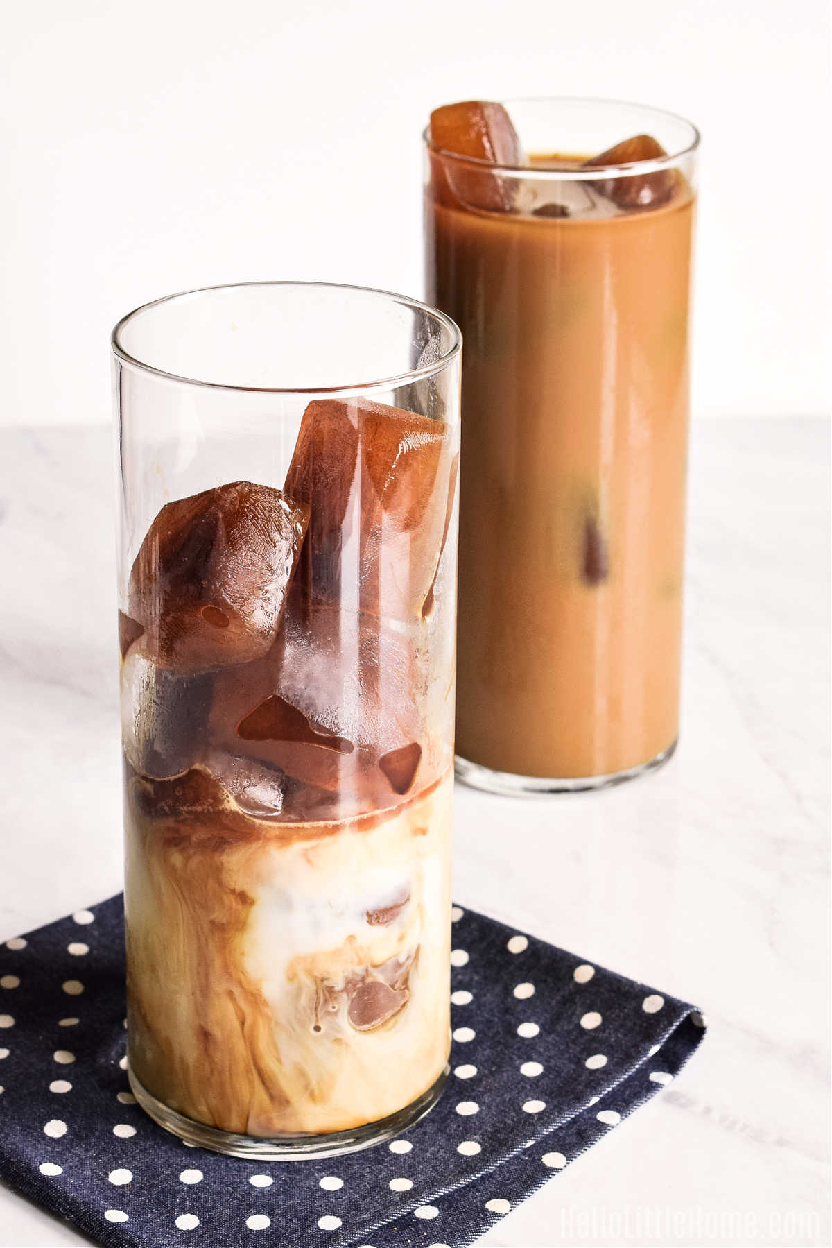 Two glasses of iced coffee on a marble counter.