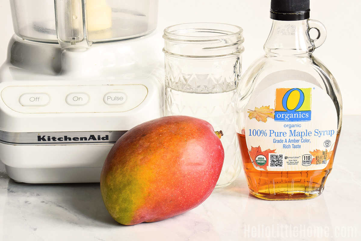 Ingredients for mango smoothie are arranged together on a marble counter.