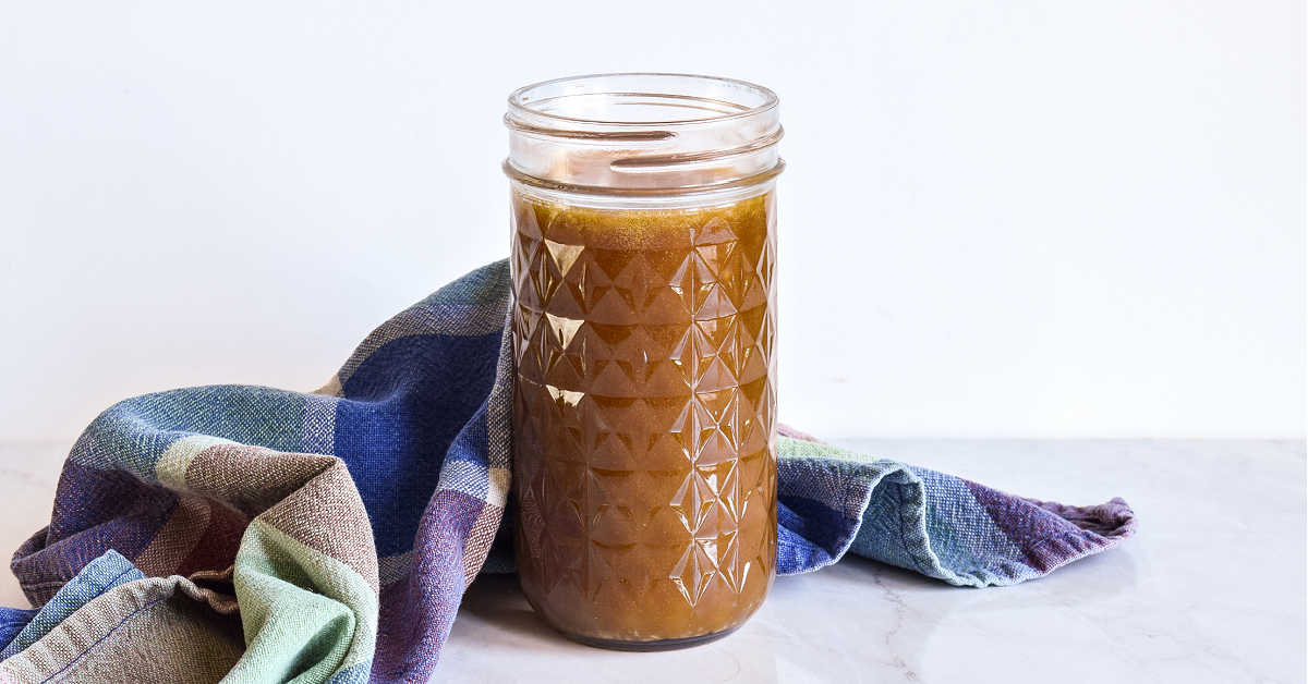 A half pint quilted mason jar of brown sugar caramel sauce on white marble beside a folded plaid dish towel