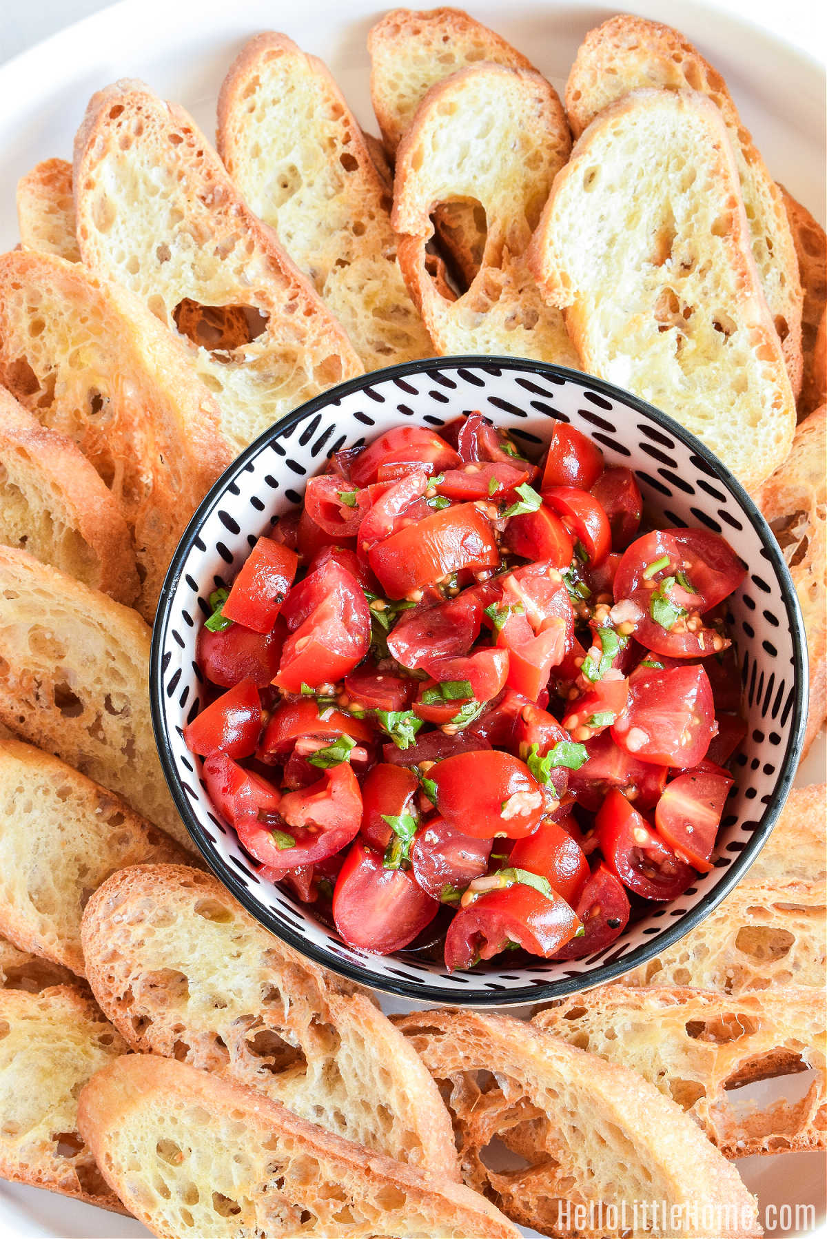 The finished crostini surrounding a bowl of tomato basil topping on a white tray.