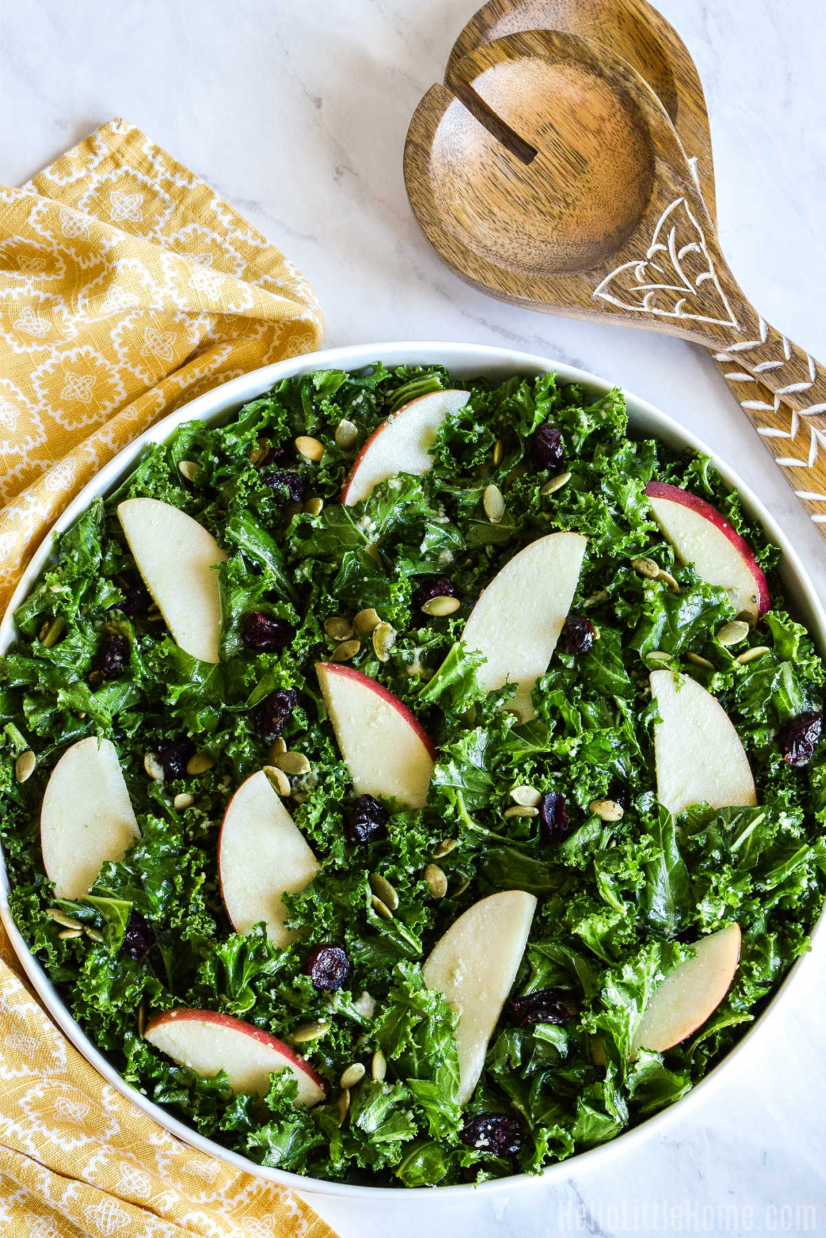 A bowl of kale salad, yellow napkin, and salad tongs on a marble table.