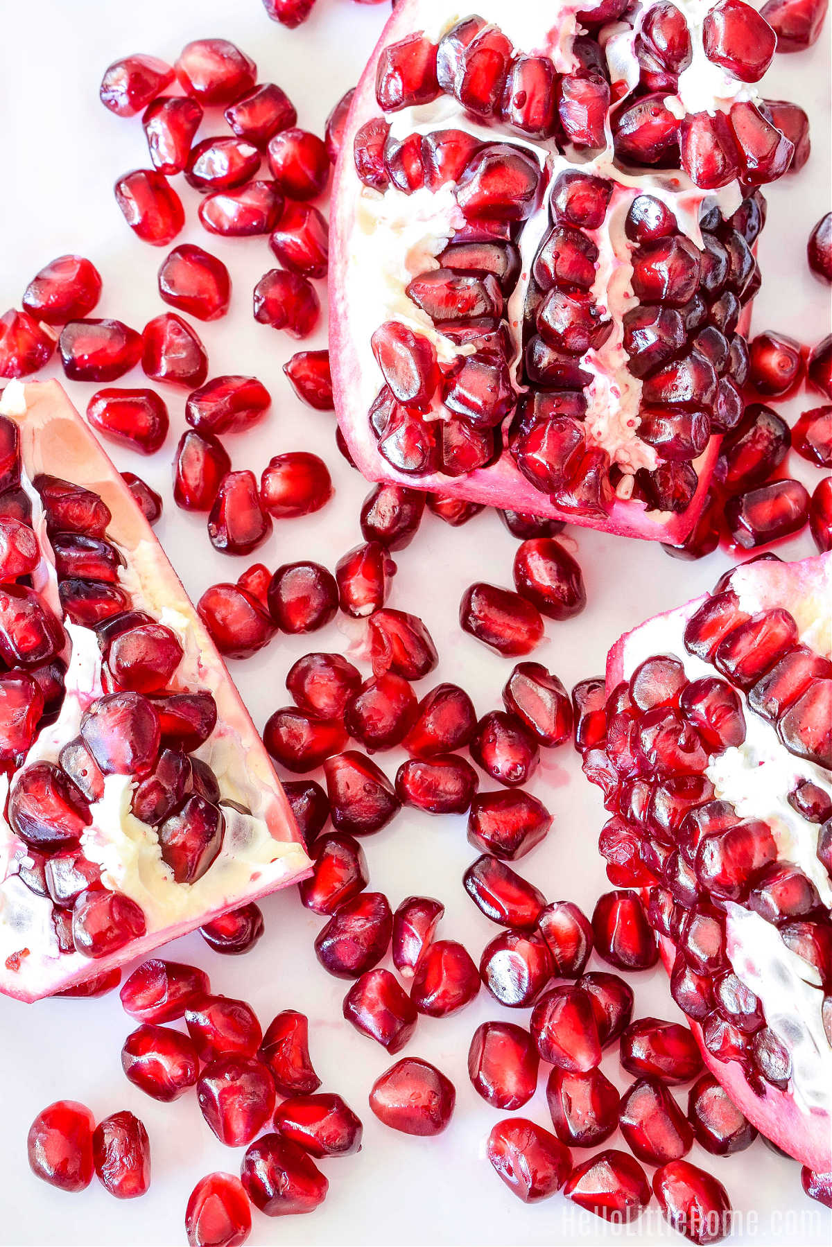 A cut pomegranate surrounded by seeds on a white plate.