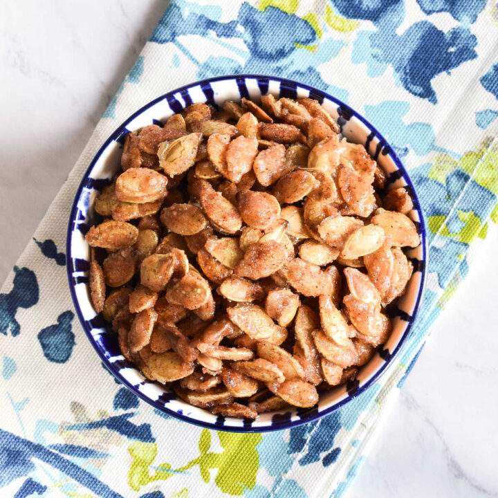 A bowl of Honey Roasted Pumpkin Seeds and a patterned napkin on a marble table.