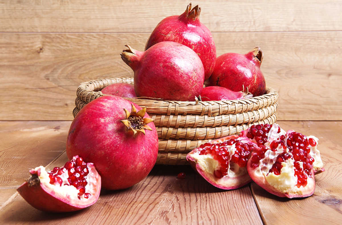 A basket filled with pomegranates on a wood table.