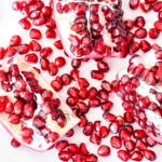 Pomegranate seeds and sections on a white plate.